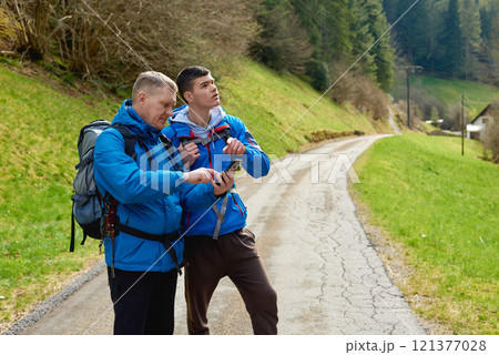 Two hikers are in the mountains in the spring nature outdoor. Hiking with backpacks. Two friends travel together in picturesque places. The man shows the way. Two men on a hiking trip in the mountains Two hikers are in the mountains in the spring nature outdoor. Hiking with backpacks. Two friends travel together in picturesque places. The man shows the way. Two men on a hiking trip in the mountains 121377028