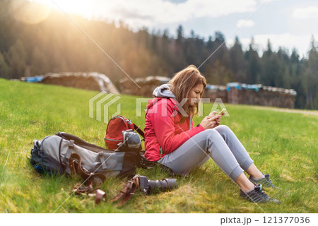 Hiking woman using smart phone. Woman traveler resting with her smartphone in the mountain forest. Spring landscape of Alps, Germany. travel and active lifestyle concept 121377036