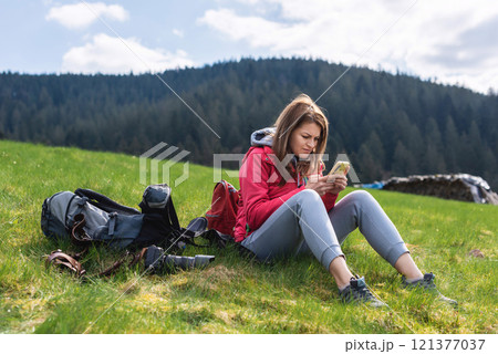 Young tourist girl resting with phone on the top of the mounting landscape. Hiking woman relaxing. Caucasian beautiful woman wearing casual clothes, adventure traveling alone and hiking on the top of 121377037