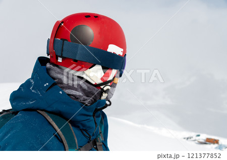Cheerful and happy man in warm blue jacket, ski mask and helmet looking away, spending extreme weekend in winter season in mountains. Portrait of sporty guy 121377852