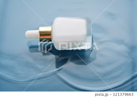 Bottle with white moisturizing serum in water on blue background. Bottle with white moisturizing serum in water on blue background. 121379663