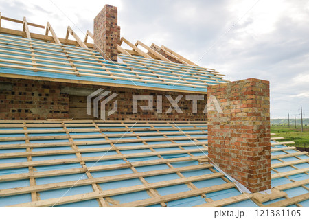 Aerial view of a brick house with wooden roof frame under construction. 121381105