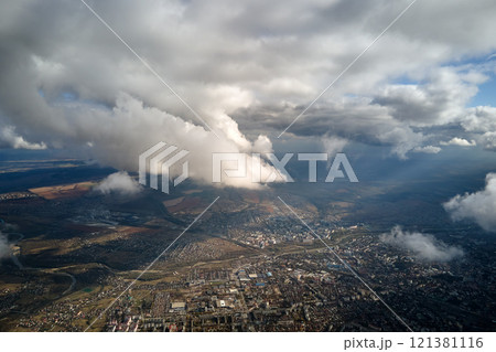 Aerial view from airplane window at high altitude of distant city covered with puffy cumulus clouds forming before rainstorm 121381116