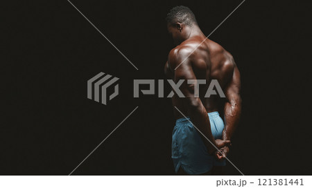 A muscular man stands with his back to the camera, showing off his physique against a dark background. 121381441
