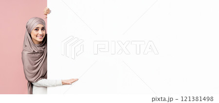 Look here. Beautiful muslim girl in hijab pointing at white blank advertisement board for your text with open palm, pink studio background Look here. Beautiful muslim girl in hijab pointing at white blank advertisement board for your text with open palm, pink studio background 121381498