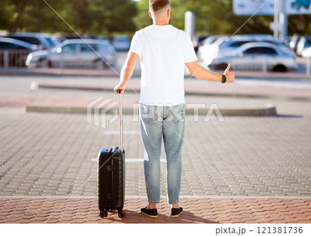 Arriving Home Concept. Tourist trying to catch taxi, standing with baggage and showing thumbs up, copyspace, back view 121381736