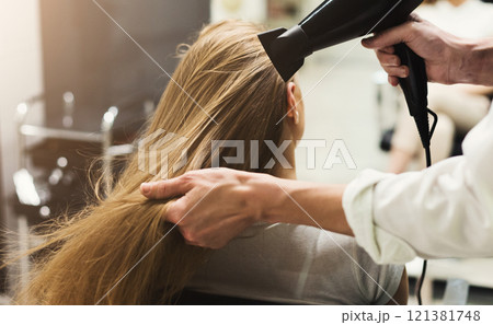 Stylist making hairstyle using hair dryer, blowing on wet customer hair at beauty salon, copy space Stylist making hairstyle using hair dryer, blowing on wet customer hair at beauty salon, copy space 121381748