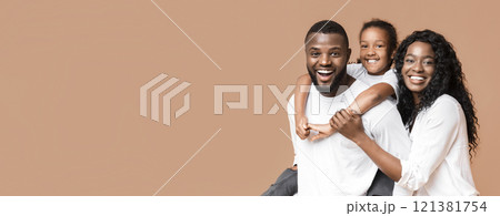 Family fun. Young african american parents spending time with their little daughter, laughing together over yellow background Family fun. Young african american parents spending time with their little daughter, laughing together over yellow background 121381754