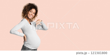 Excited afro pregnant woman pointing finger at belly, posing over white background and smiling to camera Excited afro pregnant woman pointing finger at belly, posing over white background and smiling to camera 121381800