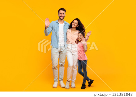 A happy family of three, a father, mother, and daughter, are standing in front of a bright yellow background. They are all smiling and waving, and they appear to be enjoying themselves. A happy family of three, a father, mother, and daughter, are standing in front of a bright yellow background. They are all smiling and waving, and they appear to be enjoying themselves. 121381848
