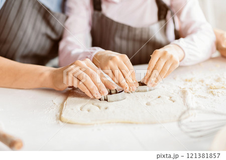 Cropped of a pair of hands using cookie cutters to cut out shapes from dough. The dough is covered in a thin layer of flour, and the cookie cutters are leaving small, perfect circles in the dough 121381857