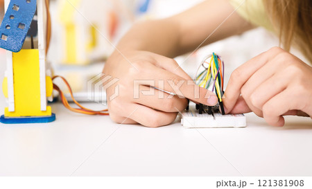 A young person is shown working on a STEM project, connecting colorful wires to a breadboard. The image captures their focused concentration as they learn about electronics and circuits. 121381908