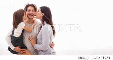 Sweetest kiss. Wife and daughter kissing happy man on both cheeks while standing together against window at home, copy space Sweetest kiss. Wife and daughter kissing happy man on both cheeks while standing together against window at home, copy space 121381924
