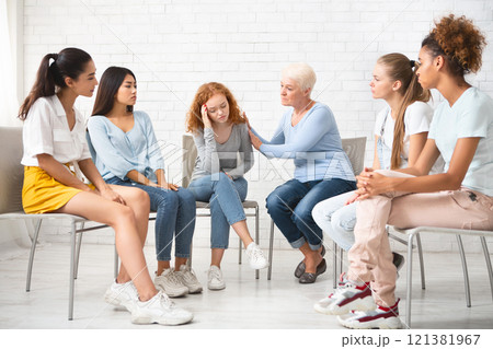 Psychologist Comforting Depressed Girl During Therapy Session With Female Support Group Sitting In Circle Indoors. Selective Focus 121381967