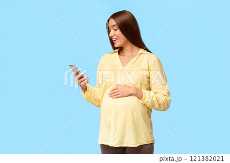 Joyful Pregnant Lady Using Cellphone Texting Standing On White Background. Pregnancy Great News. Studio Shot 121382021