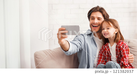 Happy moments together. Emotional young man taking selfie with his pretty little daughter at home, using smartphone, empty space 121382037