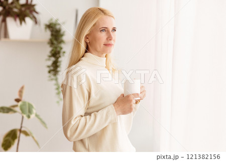 Middle-Aged Woman Drinking Coffee And Looking Through Window, Having Rest At Home Middle-Aged Woman Drinking Coffee And Looking Through Window, Having Rest At Home 121382156