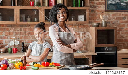 African pretty mom and daughter with arms crossed on chest smiling, cooking healthy meal together at kitchen, free space African pretty mom and daughter with arms crossed on chest smiling, cooking healthy meal together at kitchen, free space 121382157