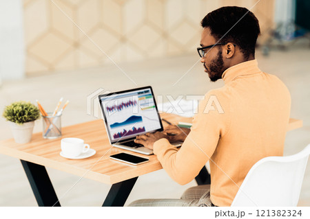Computer Screen With Graphics And Chart. Rear view of african american businessman working on laptop with graphs 121382324
