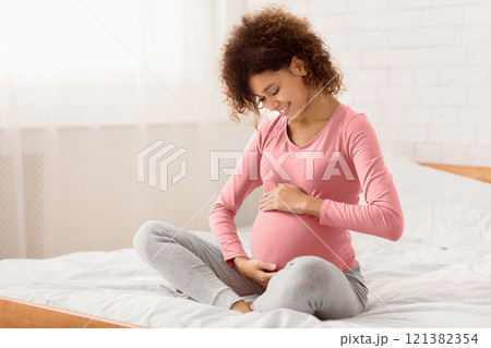 Pretty pregnant woman caressing her belly and talking to her baby, sitting on bed at home, free space Pretty pregnant woman caressing her belly and talking to her baby, sitting on bed at home, free space 121382354