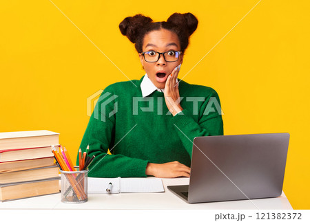 Shocking News. Surprised black teenager sitting at desk, staring at camera with opened mouth, palm on cheek. Free space 121382372