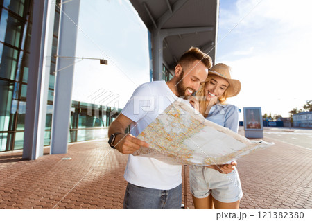 Young couple standing in front of airport terminal building, looking at map, empty space 121382380