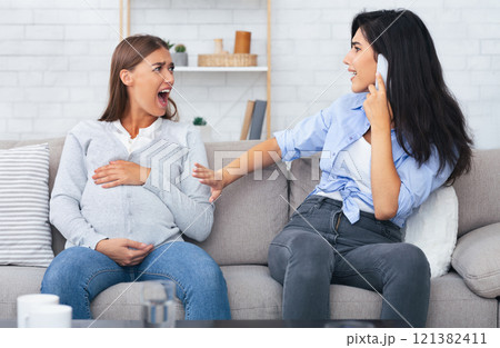 Labor And Birth. Pregnant Girl Shouting Having Painful Spasm While Her Friend Calling Doctor Sitting On Couch Indoor. 121382411