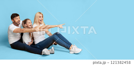 A family of three, a man, a woman, and a young girl, are seated on a light blue background. They are all pointing to the copy space, smiling, and looking excited, panorama A family of three, a man, a woman, and a young girl, are seated on a light blue background. They are all pointing to the copy space, smiling, and looking excited, panorama 121382458