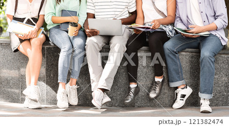 Studying Outdoors. Group of college students sitting with laptop and books, preparing for lectures together, crop 121382474