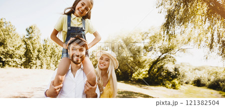 Family walk. Parents play with his daughters outdoors, girl sitting on father shoulders Family walk. Parents play with his daughters outdoors, girl sitting on father shoulders 121382504