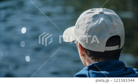A person sits quietly by the water's edge, gazing out at the shimmering lake and reflecting on nature's beauty. 121383344