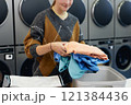 Cropped shot of young woman holding pile of colored clothes sorting delicate garment before loading into washing machine in self service laundry, copy space 121384436