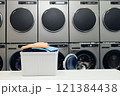Background shot of basket full of colored clothes on folding table in self service laundry with professional dryers and washing machines, copy space 121384438