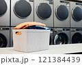 Still life shot of plastic basket full of clean folded clothes on table in self service laundry with professional equipment, copy space 121384439