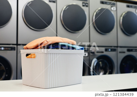 Still life shot of plastic basket full of clean folded clothes on table in self service laundry with professional equipment, copy space 121384439