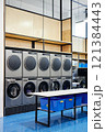 Interior of modern self service laundry featuring double row of professional washing machines and clothes dryers nest to folding table, copy space 121384443