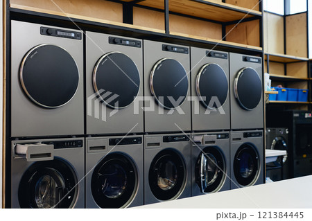 Double row of professional washing machines and coin operated clothes dryers at self service laundromat, copy space 121384445