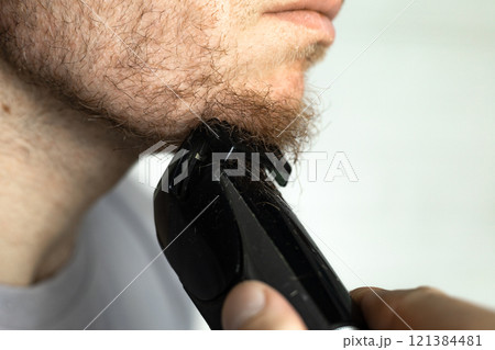A man trims his beard with a trimmer. An electric razor trimming a beard. A man trims his beard with a trimmer. An electric razor trimming a beard. 121384481