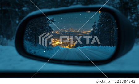 A snowy road stretches ahead, while the side mirror reflects a beautifully lit city in the distance during the evening. Soft snowflakes fall gently, creating a serene winter atmosphere. A snowy road stretches ahead, while the side mirror reflects a beautifully lit city in the distance during the evening. Soft snowflakes fall gently, creating a serene winter atmosphere. 121384542