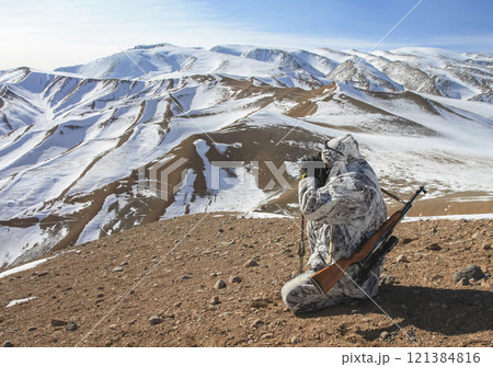 Hunter looks through binoculars against background of sky and mountain landscape. Hunter looks through binoculars against background of sky and mountain landscape. 121384816
