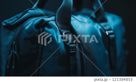 A black backpack is highlighted in low light, emphasizing the texture of the fabric and the design of the straps. The dark setting adds an intriguing contrast, enhancing its features. 121384853