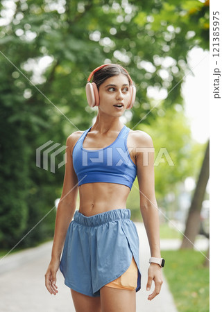 A young woman jogs in nature, wearing headphones and enjoying the vibrant surroundings A young woman jogs in nature, wearing headphones and enjoying the vibrant surroundings 121385975