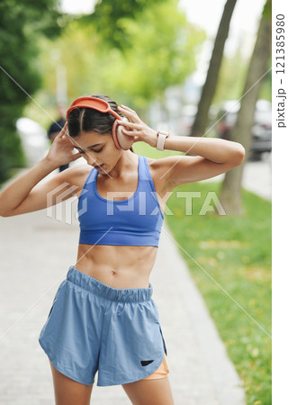 An Active Young Woman is Happily Enjoying Her Music While Exercising in the Outdoors 121385980