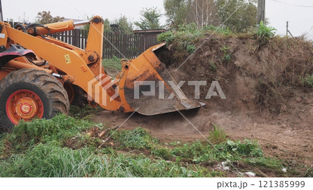 A heavy excavator is actively clearing soil and debris at a construction site, displaying powerful machinery in action 121385999
