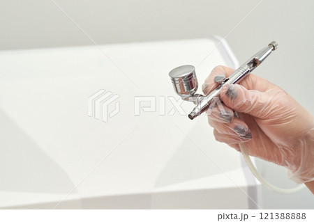 Gloved hand using airbrush against white background for precise artistic 121388888