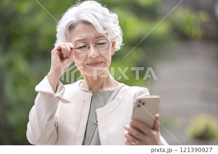 目を細めてスマホの画面を見るシニア女性 目を細めてスマホの画面を見るシニア女性 121390927