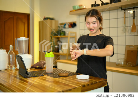 Beautiful asian woman drinking protein shake after workout and checking her smartwatch Beautiful asian woman drinking protein shake after workout and checking her smartwatch 121390982