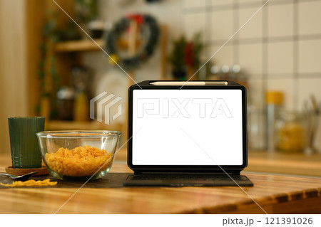 Front view digital tablet with white screen near a bowl of cornflakes on kitchen table 121391026