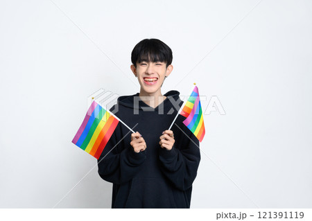 Cheerful man holding two small rainbow pride flags against white background. LGBTQ pride and equality concept Cheerful man holding two small rainbow pride flags against white background. LGBTQ pride and equality concept 121391119