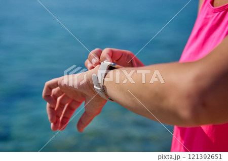 Female athlete using fitness watch while running on sunny day 121392651